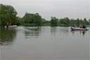 picture of two boats, black newfoundland dog is swimming from one boat to other carrying a rope